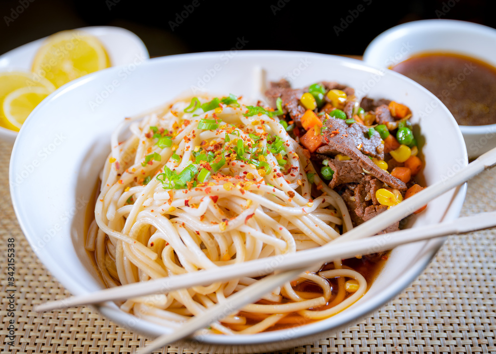 Noodles con carne en plato blanco con verduras y complementos 