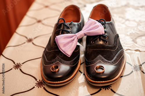 Pair of gold wedding rings and pink bowtie on the black shoes