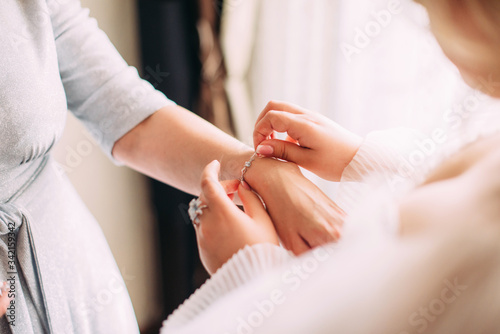 A bride puts a bracelet on her mom's arms close-up at her wedding, morning gatherings