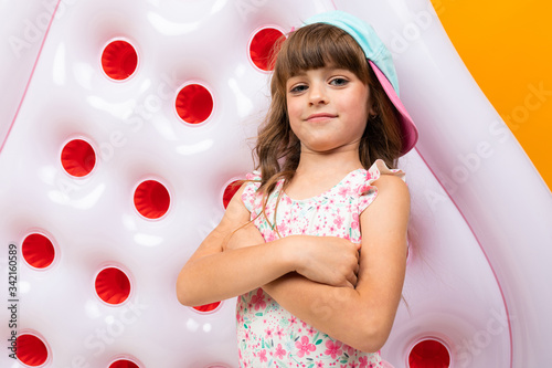 Beautiful little girl in swinsuit holds a rubber mattress and smiles isolated on yellow and orange background photo