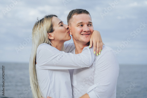 Charming young woman embracing with boyfriend on sea background. Outdoor photo of happy couple standing near ocean. Summer vacation concept. Casual style. Happy together. Outdoor shot