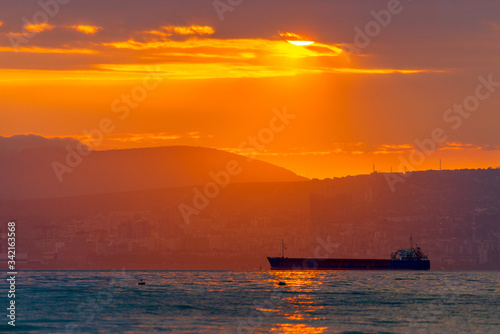 Cargo ship sailing the sea at a golden sunset or sunrise. Ocean shipment across water as the sun sets or rises. Harmony and beauty in nature. Scenic peaceful sea view © rostovdriver