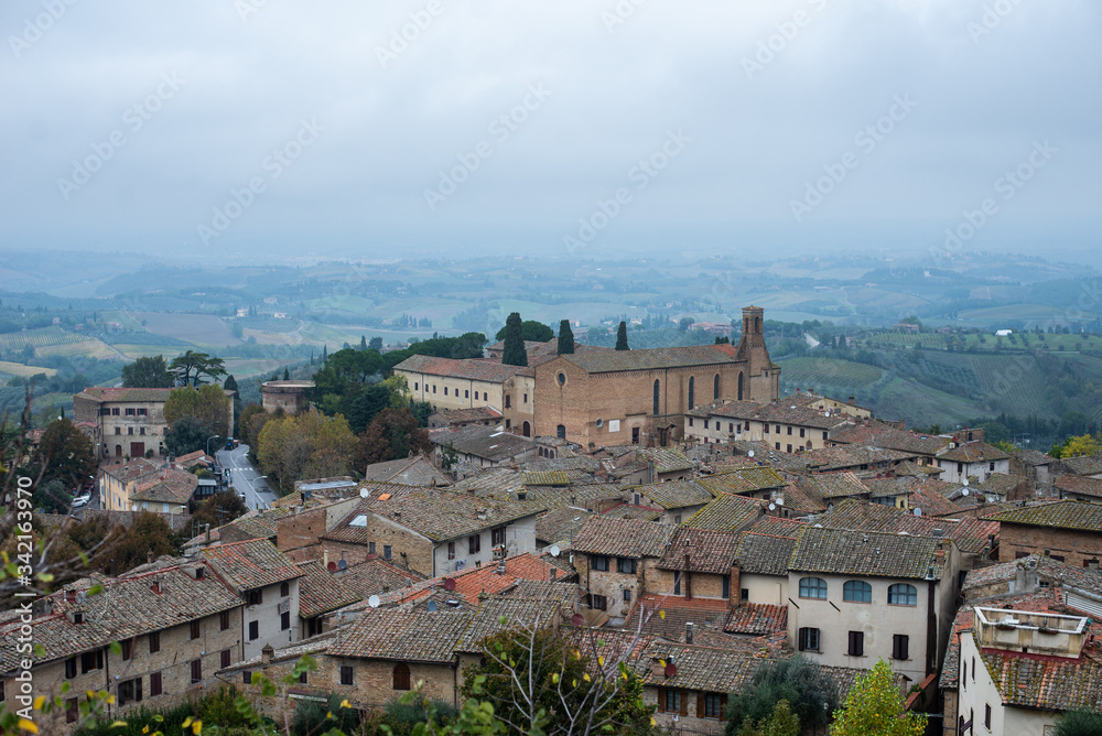 Famous place in Tuscany Italy.Medieval architecture of italian city.Panoramic view of rooftop cityscape and foggy landscape in background.Rainy autumn day in San Gimignano.Popular tourist destination