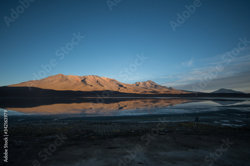 Panorama of Andean peaks reflecting in laguna during sunset with bright blue sky