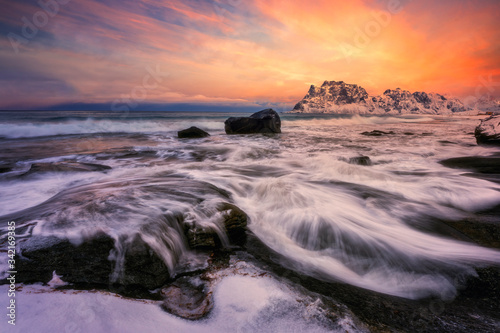 Dramatic sunset at beach, with waves washing over coastal rocks.