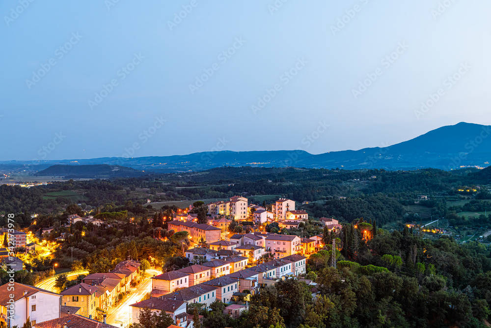 Chiusi town village at night in Tuscany, Italy with illuminated lights on streets and rooftop houses on mountain countryside and rolling hills