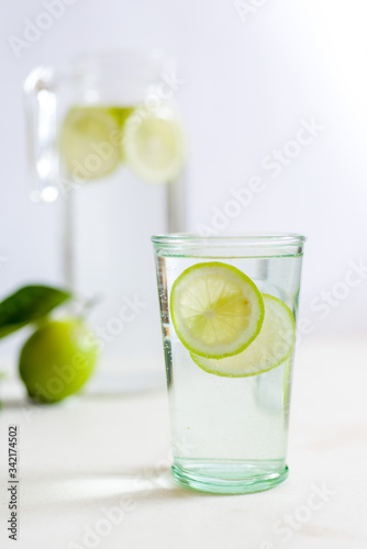 Closeup glass of warm water with lime with a jug and whole fresh lime on the background 