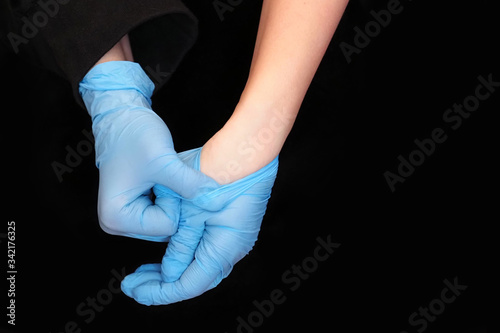 Woman takes off medical gloves on black background. Quarantine end concept