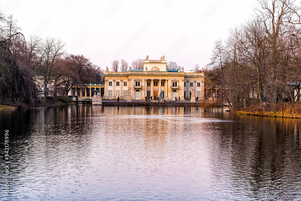 Warszawa Lazienki or Royal Baths Park garden with palace building in center by water lake at sunset in Warsaw, Poland with people walking by Christmas tree