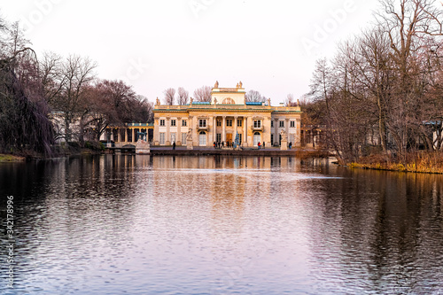 Warszawa Lazienki or Royal Baths Park garden with palace building in center by water lake at sunset in Warsaw, Poland with people walking by Christmas tree