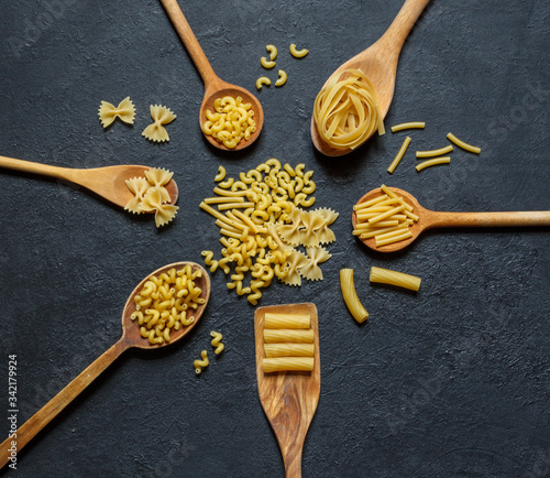 Different types of dry pasta on wooden spoons on top on a black background photo