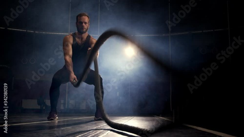 Male athlete training using battle ropes workout exercise. Black background. photo