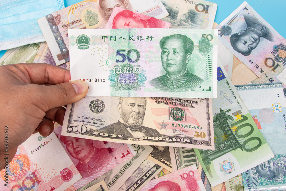 Obraz premium Man Hand holding Bank Note of YUAN RMB and USD Dollar with World banknotes collection mixed on table, top view. Business and finance concept.