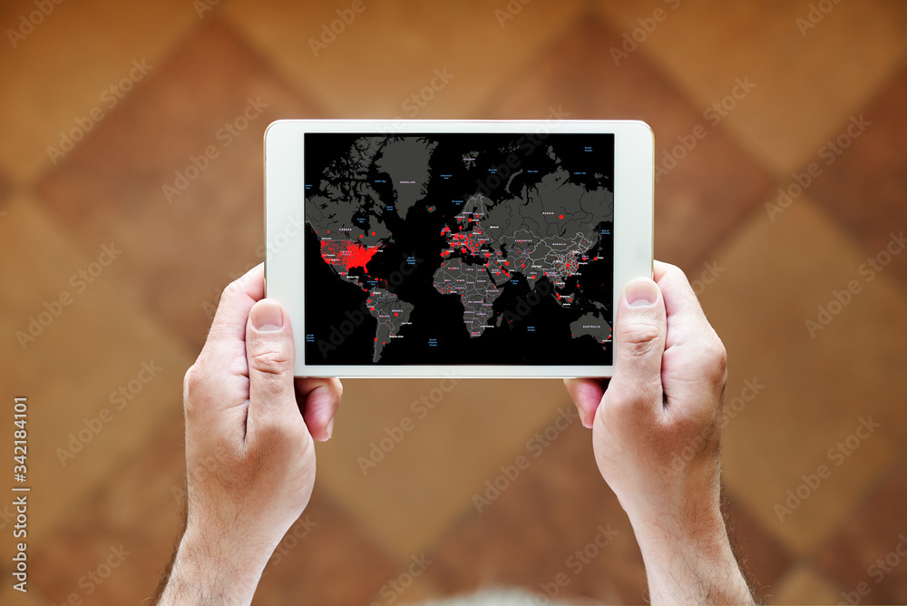 a man holding a tablet in his hands with a distribution map of coronavirus or covid-19, standing at home near the window, top view a man holding a tablet in his hands with a distribution map of coronavirus or covid-19, standing at home near the window, top view