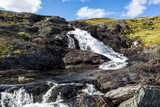 Sunny white scenic norwegian powerful river cascade waterfall with dark rocks and bright blue sky. Nature travel clean falling water landscape