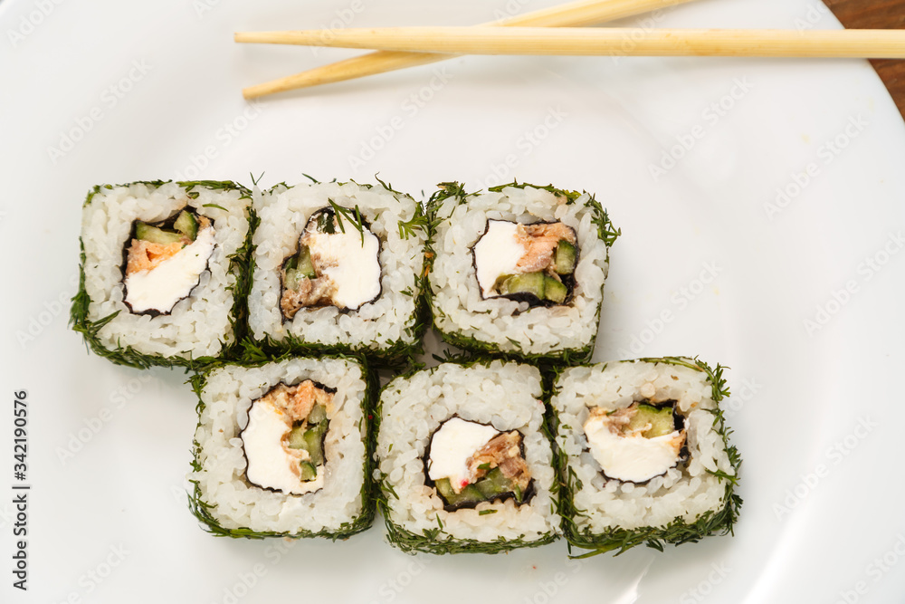 Rolls with salmon and dill on a white plate with chopsticks. Rolls with salmon and dill on a white plate with chopsticks.