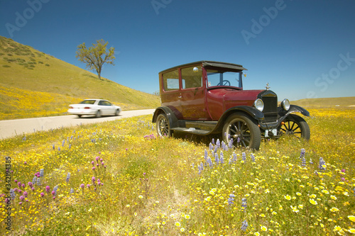 A modern car driving by a maroon Model T parked alongside a scenic road surrounded by spring flowers,  Route 58, Shell Road, CA