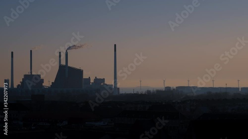 Silhouette of a powerplant in Copenhagen turned into a skislope, with a tall smoking chimney, in sunrise in calm weather with windturbines and the sea in the background. photo