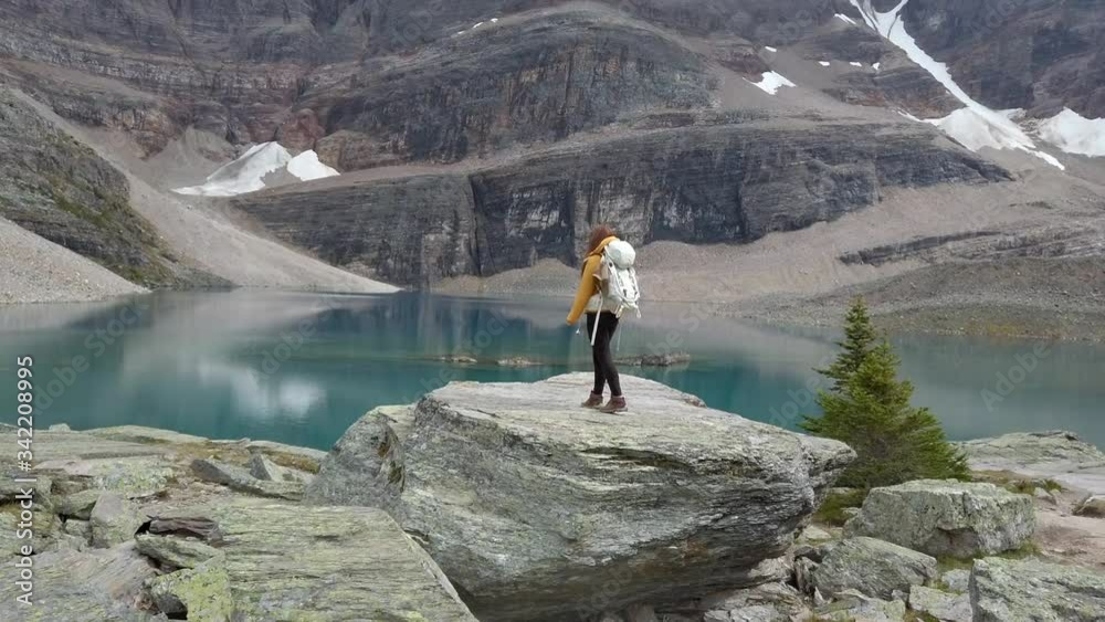 A woman hiker stands on a huge boulder taking in the majestic reflections of Oesa Lake, Alberta, Canada. A woman hiker stands on a huge boulder taking in the majestic reflections of Oesa Lake, Alberta, Canada.