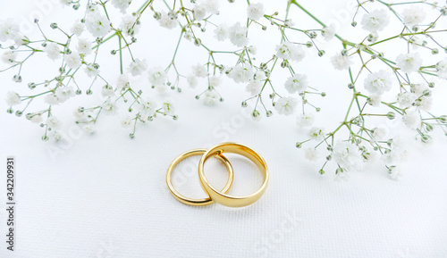 Wedding background with gold rings and small flowers s on white fabric. Wedding invitation background.
