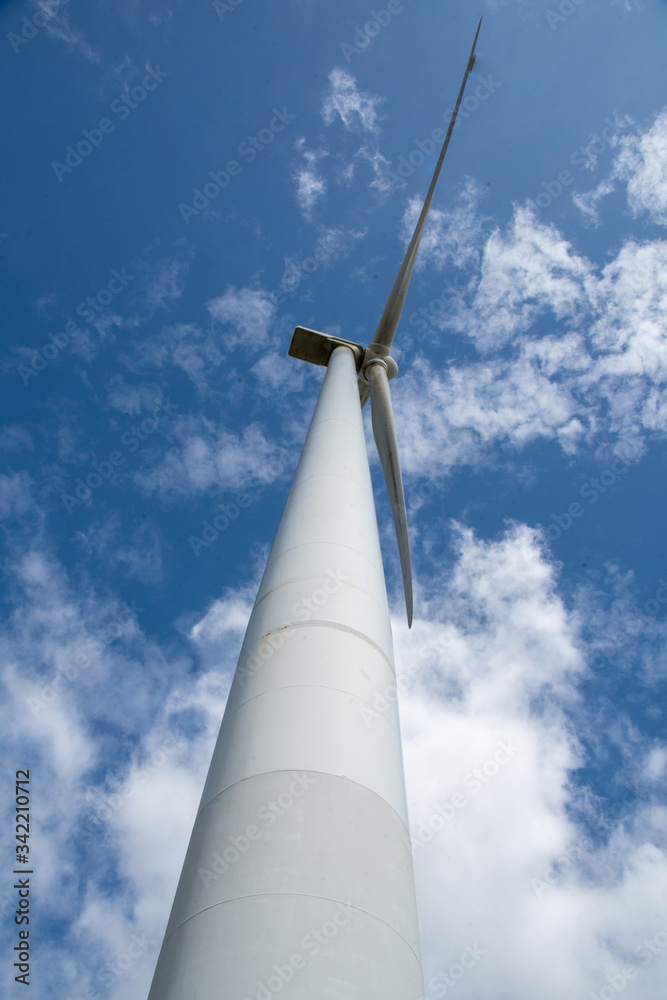 Portrait of a huge electricity generating wind turbine tower and blades in a wind farm in nature being driven by the wind Portrait of a huge electricity generating wind turbine tower and blades in a wind farm in nature being driven by the wind