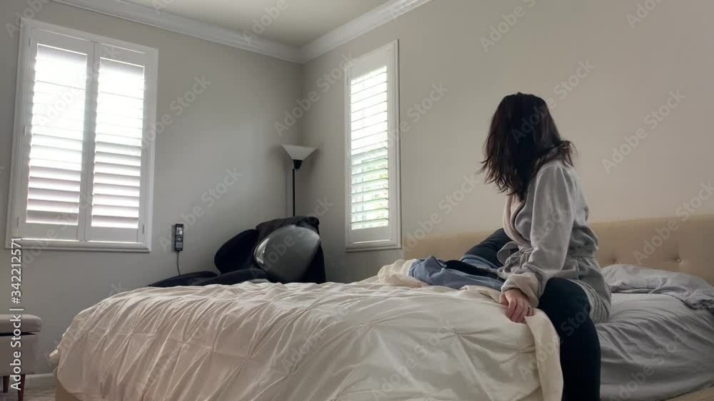 Woman getting ready for a brand new start to a day. She stretches, gets up and out of bed, and fixes her bed coverings. White simple room with natural sunlight shining through window blinds. Woman getting ready for a brand new start to a day. She stretches, gets up and out of bed, and fixes her bed coverings. White simple room with natural sunlight shining through window blinds.