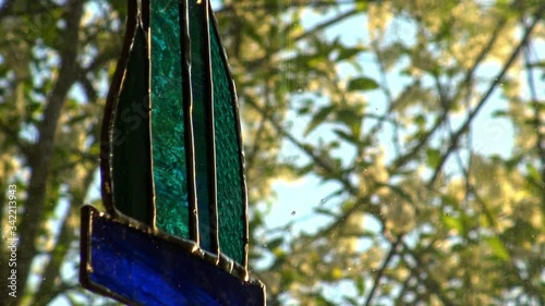 Stained glass suncatcher ornament hung up in a window glistening in the morning sun with spring blossom and leaves blowing in the bokeh background. photo