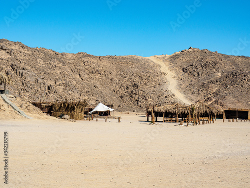 Bedouin village in egyptian desert, long view. Clear blue sky over grey mountain. Reed shacks befor mountain. Selective soft focus. Blurred background