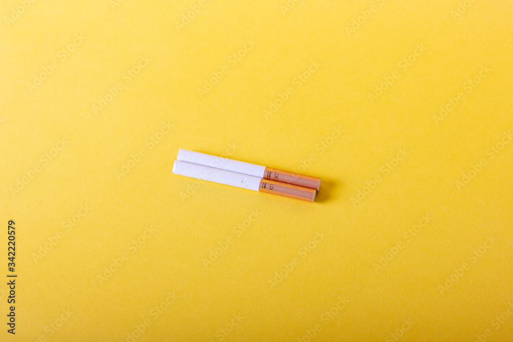 Two cigarettes stand on a yellow background Two cigarettes stand on a yellow background