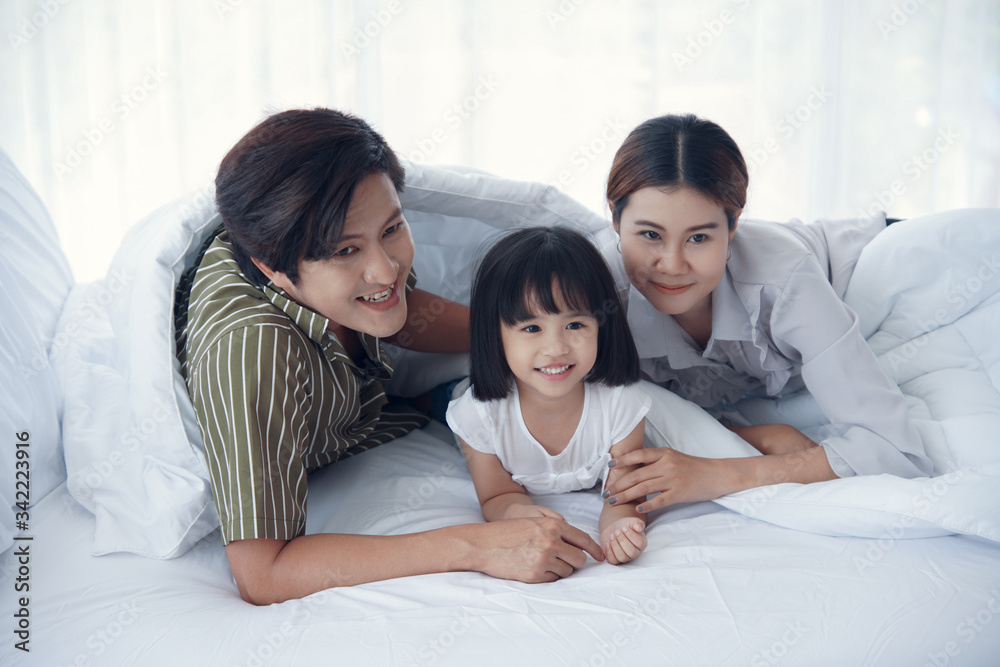 Happy asian family with a daughter are lying on the bed. They are smiling and looking at the camera Happy asian family with a daughter are lying on the bed. They are smiling and looking at the camera