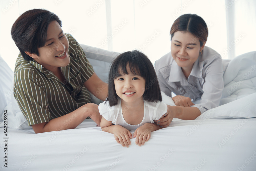 Happy asian family with a daughter are lying on the bed. They are smiling and looking at the camera. Happy asian family with a daughter are lying on the bed. They are smiling and looking at the camera.
