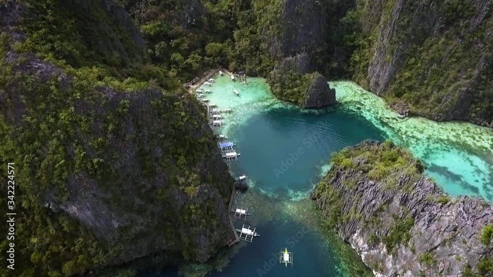 High aerial descending looking down drone view above lime stone mountain cliff, green turquoise water, boat pier and boat sailing inside the lagoon, Philippines High aerial descending looking down drone view above lime stone mountain cliff, green turquoise water, boat pier and boat sailing inside the lagoon, Philippines