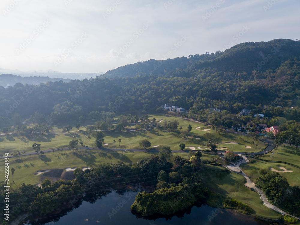 Beautiful lake located on a golf course surrounded by houses and mountains at dawn, photo from a drone. In the lake the reflection of the sky. Great background for travel and golf advertising.