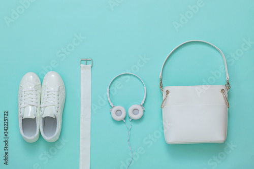 White sneakers, white headphones, white belt and white bag on a light background. Flat lay.