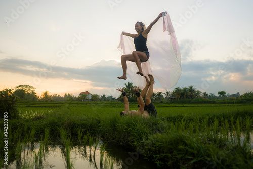 Fototapeta Naklejka Na Ścianę i Meble -  outdoors sunset acroyoga workout - young happy and fit couple practicing acro yoga drill at beautiful rice field enjoying nature doing acrobatic pose with woman in wings
