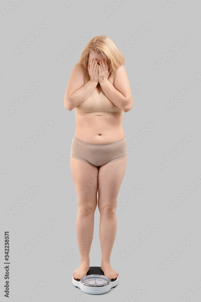 Obraz premium Sad overweight woman with scales on grey background. Weight loss concept