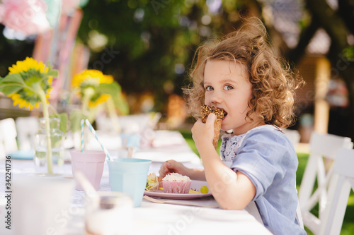 Small girl sitting outdoors in garden in summer, eating snacks.