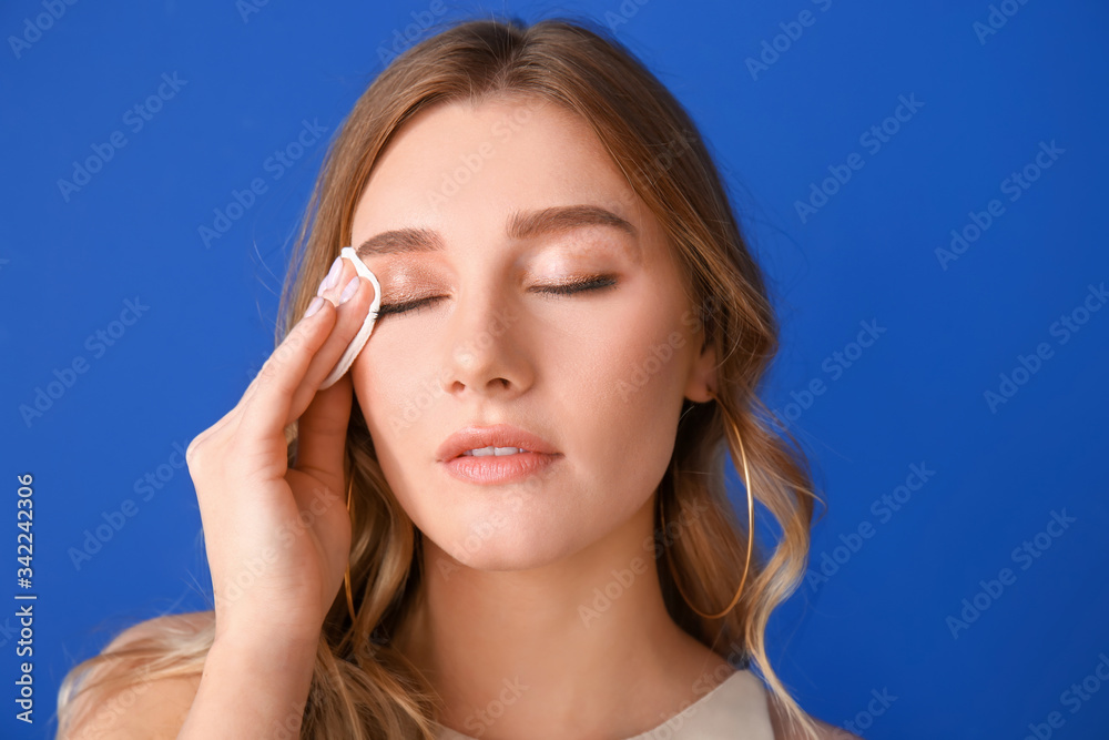 Beautiful young woman removing makeup against color background Beautiful young woman removing makeup against color background