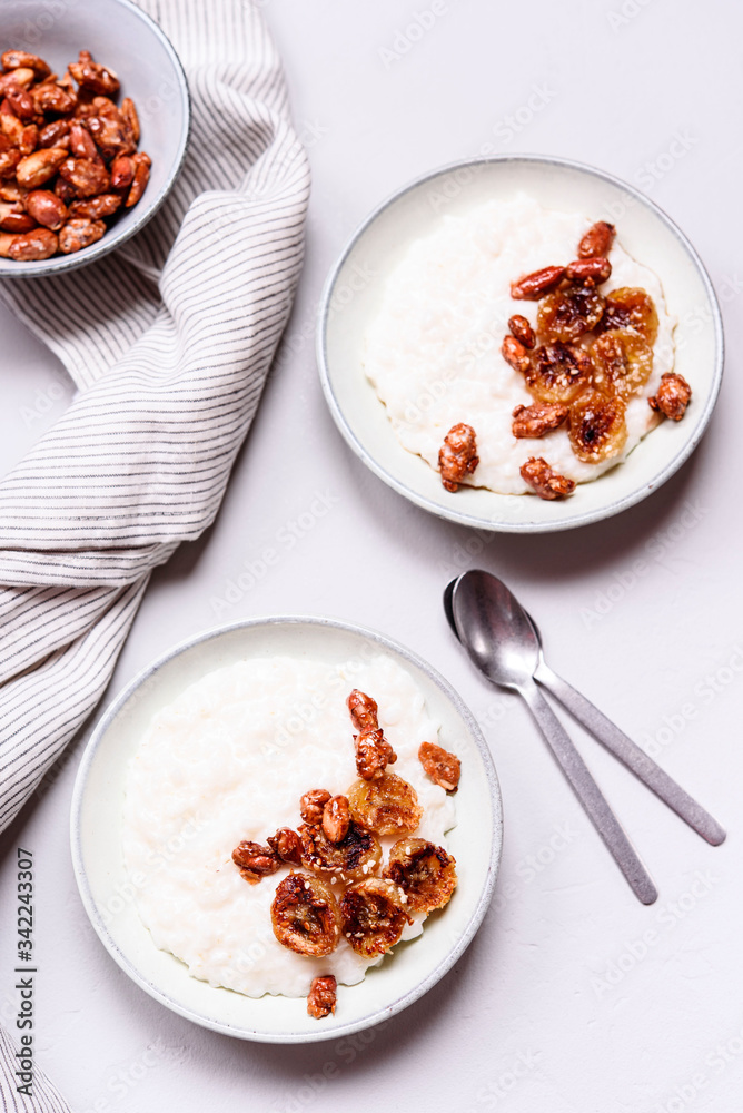 Creamy Rice Porridge or Pudding with caramelized bananas and nuts in bowls on grey concrete background. Selective focus Creamy Rice Porridge or Pudding with caramelized bananas and nuts in bowls on grey concrete background. Selective focus