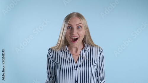 Blonde female widely opening her mouth in astonishment. Blue background.