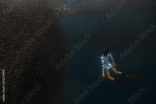 Young female in a sexy swimwear dives into a massive school of sardines using long diving fins. Moalboa, Cebu, Philippines.