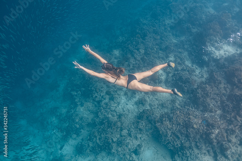 Young female in a sexy swimwear dives into a massive school of sardines using long diving fins. Moalboa, Cebu, Philippines.