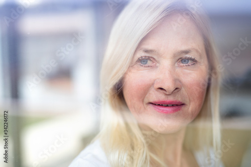 Portrait of senior woman standing indoors at home. Shot through glass.