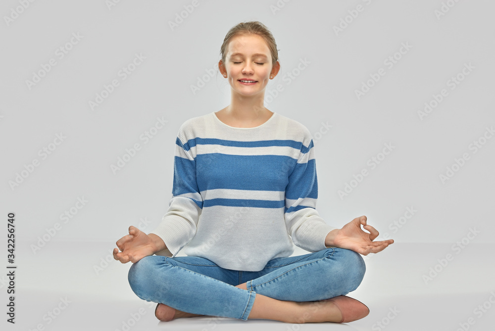 mindfulness, spirituality and people concept - smiling teenage girl in pullover meditating in lotus pose sitting on floor over grey background mindfulness, spirituality and people concept - smiling teenage girl in pullover meditating in lotus pose sitting on floor over grey background