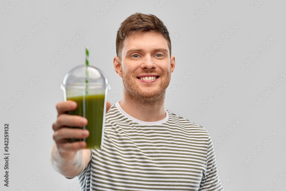 healthy eating and people concept - happy smiling man drinking green smoothie from disposable plastic cup with paper straw on grey background healthy eating and people concept - happy smiling man drinking green smoothie from disposable plastic cup with paper straw on grey background