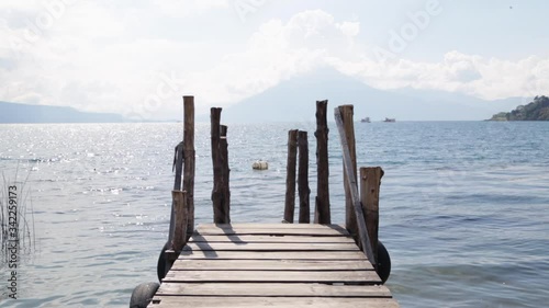 rustic wooden pier in lake atitlan, guatemala - blue sky landscape with clouds over panajachel lake with background volcano and blue sky photo