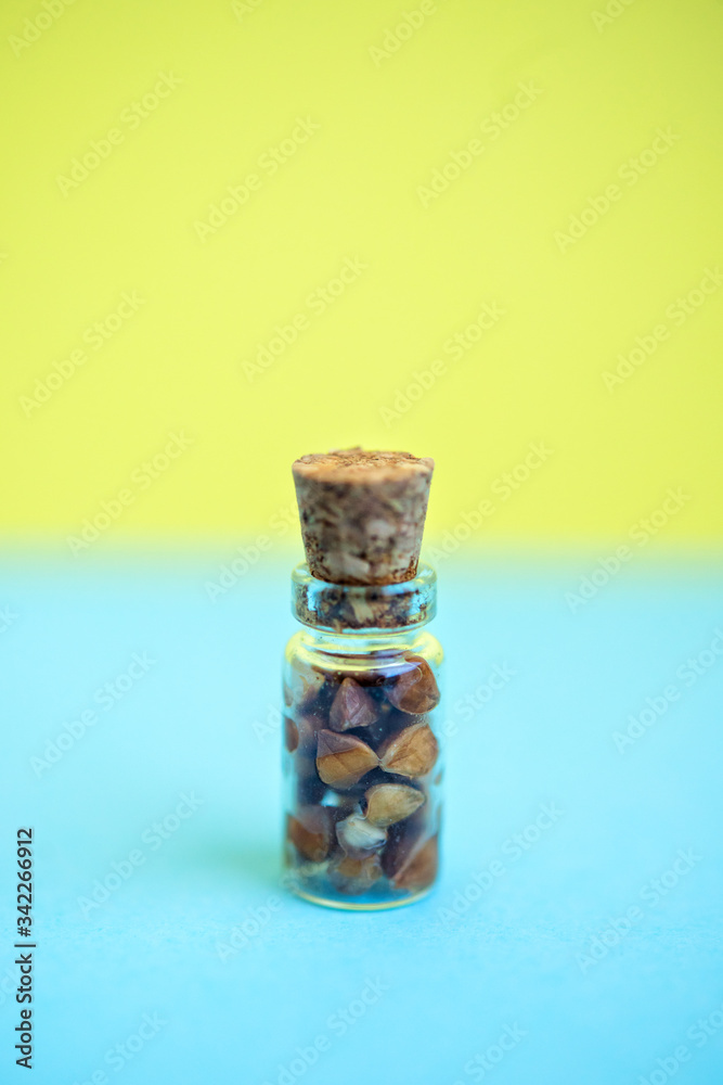 Vertical picture with soft focus of tiny glass jar with buckwheat on blue and yellow background, side view. Concept of healthy nutrition, diet, vegetarian products. Empty space for text and design Vertical picture with soft focus of tiny glass jar with buckwheat on blue and yellow background, side view. Concept of healthy nutrition, diet, vegetarian products. Empty space for text and design