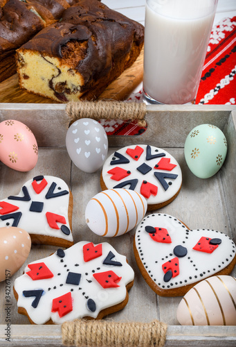 Slices of Romanian sponge cake or chec, cozonac with red traditional towel with manual stitch on wooden board, Easter painted eggs and home made ginger bread hearts, Authentic Easter Brunch concept.  photo