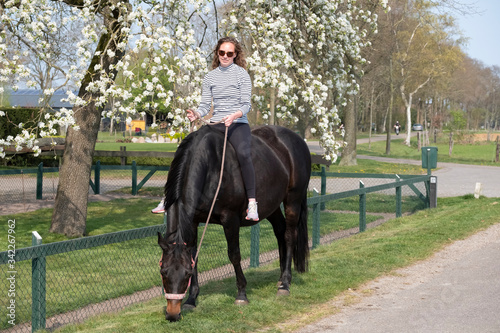 Girl on a pregnant brown horse without a saddle, with white blossom in the background