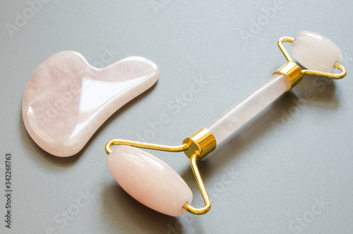 Pink Gua Sha massage tool on a gray background. Rose Quartz roller. Facial skin care at home, anti-aging and lifting therapy. - Image © ireneromanova